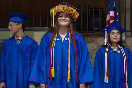 Tres estudiantes de la Hawaiian Mission Academy en togas de graduación azules frente a un edificio de piedra.