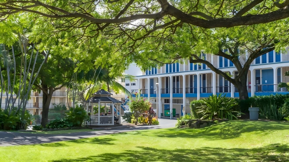 Un jardín verde con un pabellón y un edificio azul y blanco en el terreno de la Hawaiian Mission Academy.