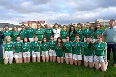Un grupo de jóvenes atletas en uniforme verde posan juntas en un campo en el campus del Hazelwood College.