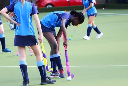 Un grupo de jóvenes atletas juega hockey en el campo de césped artificial durante la clase de educación física de la Headington School.