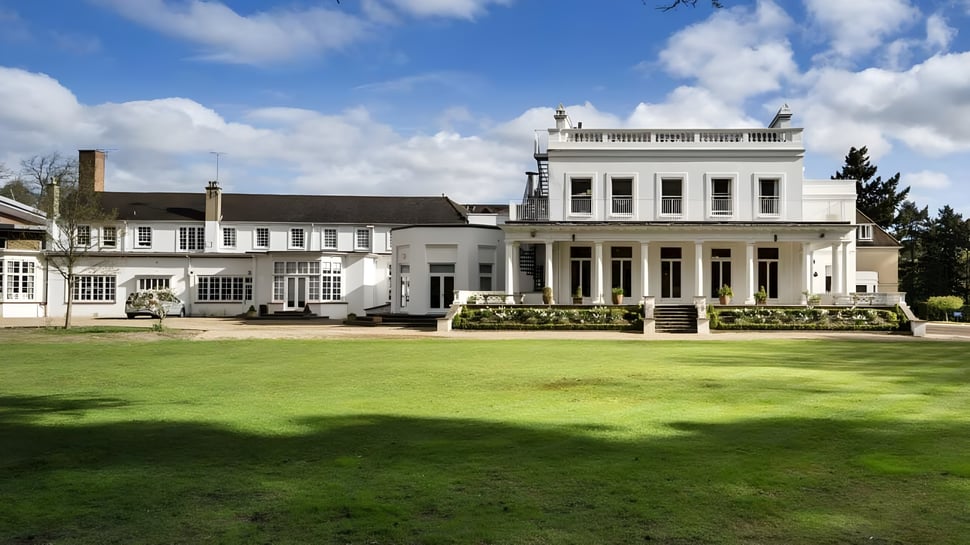 La mansión blanca con columnas en la entrada se encuentra en el terreno de la Heathfield School en Ascot frente a un césped verde y un cielo azul.
