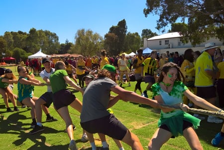 Estudiantes de la Henley High School se reúnen en un campo durante un festival con trajes coloridos y carpas.