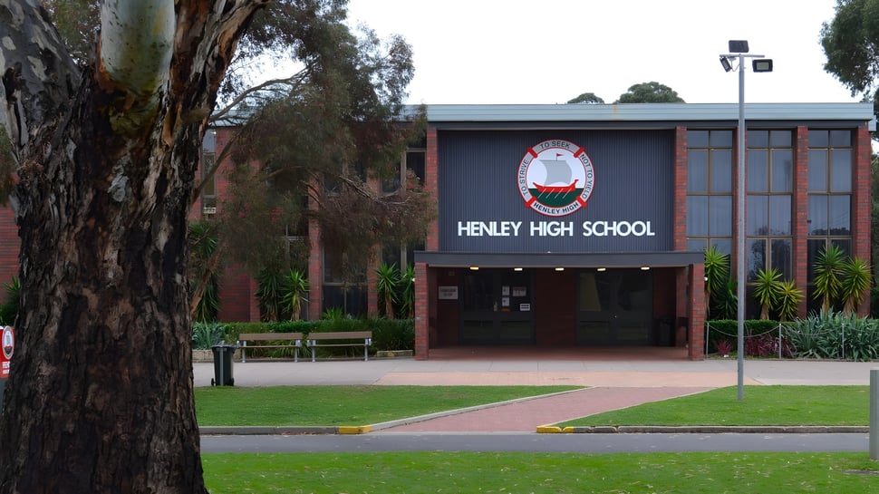 La entrada del edificio de ladrillo de la Henley High School con un gran letrero y árboles en primer plano.
