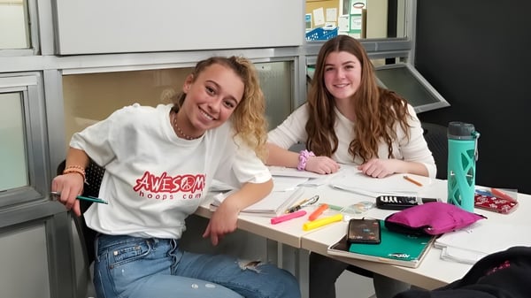 Dos estudiantes de la Henry Wise Wood High School están sentadas en una mesa y estudian juntas con materiales escolares.