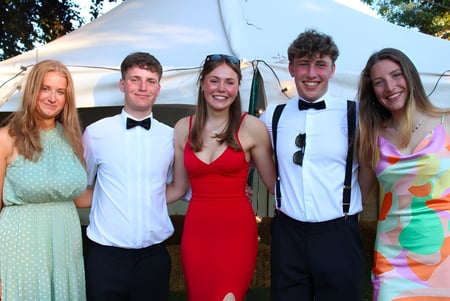 Un grupo de cinco estudiantes de la Hereford Cathedral School está frente a una tienda al aire libre con árboles de fondo.