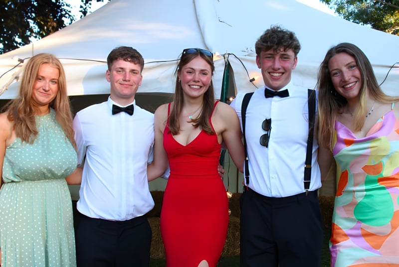 Un grupo de cinco estudiantes de la Hereford Cathedral School está frente a una tienda al aire libre con árboles de fondo.