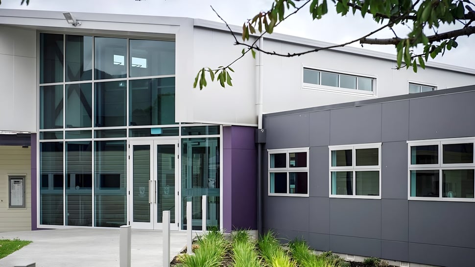 El moderno y de varios pisos edificio principal del Heretaunga College con paredes de vidrio y acentos morados está rodeado de árboles.