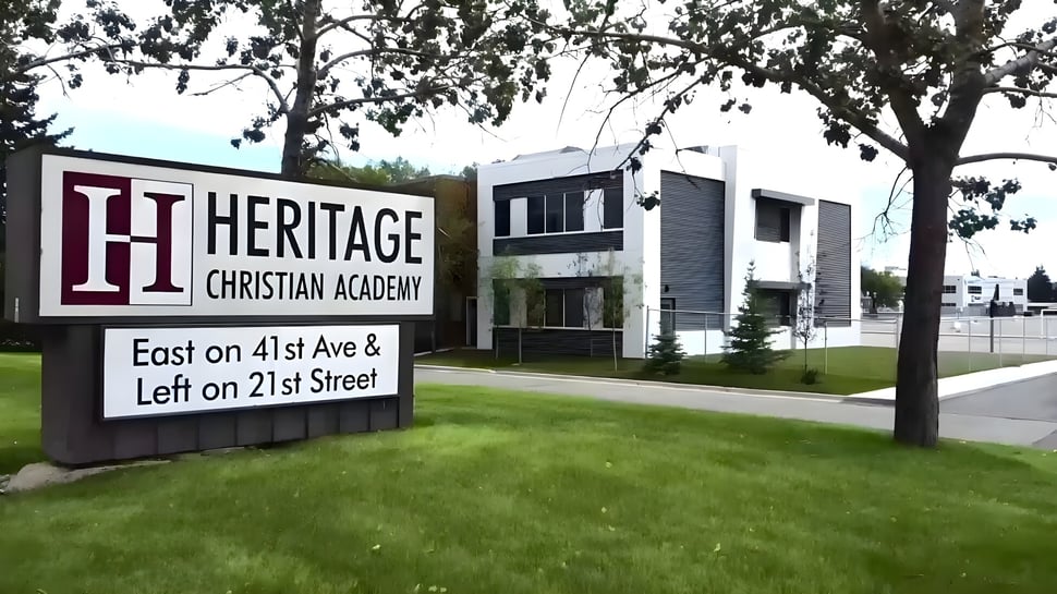 El gran cartel de la Heritage Christian Academy con edificio escolar y campo de césped al fondo.