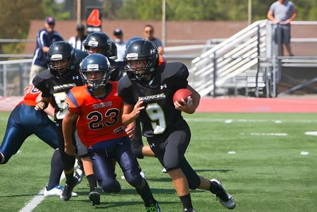 Estudiantes de la Heritage Christian School juegan al fútbol en el campo deportivo con espectadores al fondo.