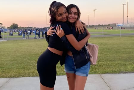Dos estudiantes se abrazan en un prado frente al estadio deportivo de la Heritage High School.