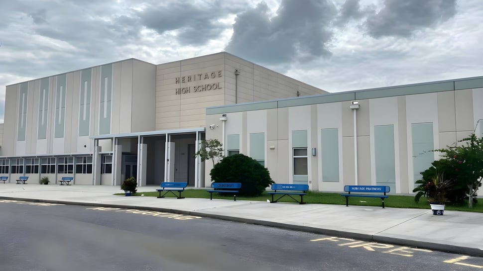 El edificio escolar de varios pisos de la Heritage High School con un letrero en la fachada bajo un cielo nublado.