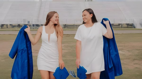 Dos estudiantes de la Heritage High School están juntas afuera frente a una gran arena y sonríen.