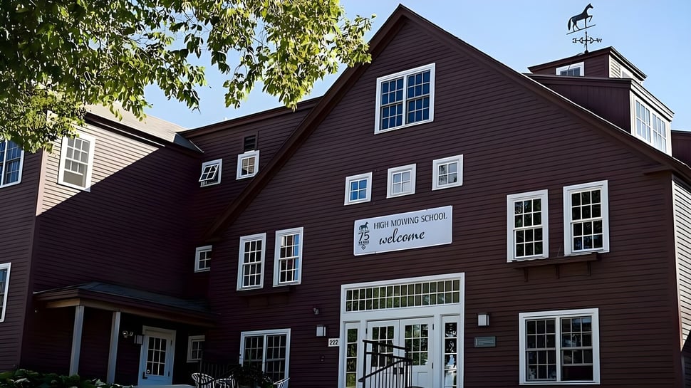 El edificio de madera de dos pisos de la High Mowing School está rodeado de un exuberante verde y cielo azul.