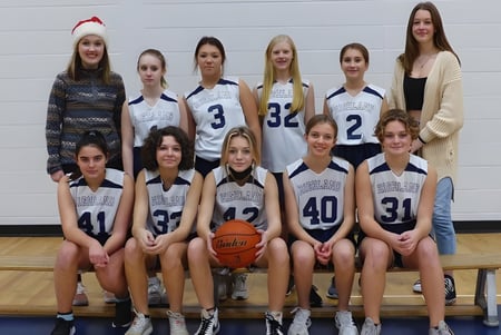 Un grupo de jóvenes jugadoras de baloncesto de la Highland Secondary School posan juntas en el gimnasio con un balón de baloncesto.