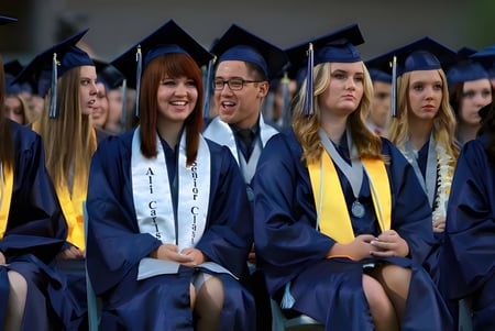 Estudiantes del Higley Unified School District llevan togas de graduación azules y amarillas y están sentados juntos en un auditorio.