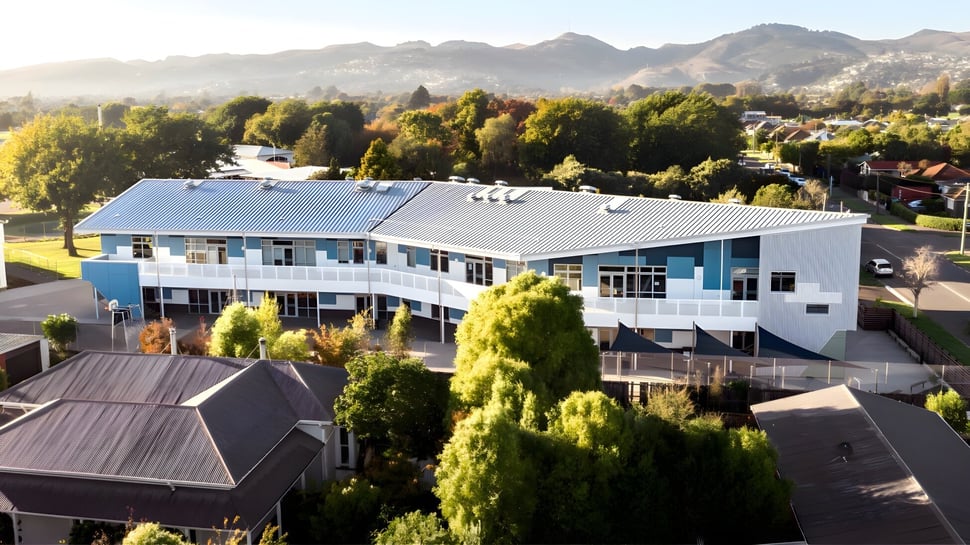 El moderno edificio de varios pisos de la Hillmorton High School está rodeado de un paisaje verde con montañas al fondo.