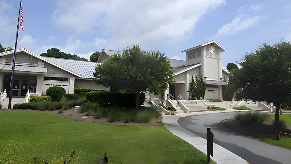 El bien cuidado edificio de la Hilton Head Preparatory School con techo de metal y una alta chimenea se encuentra en un área de césped junto a un camino pavimentado.