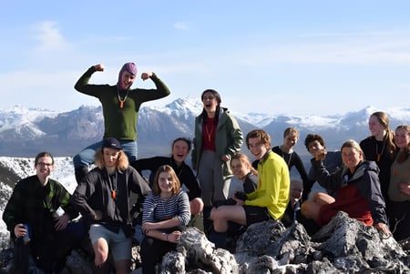 Un grupo de estudiantes de la Hobart City High School posa sobre una roca con montañas nevadas de fondo.
