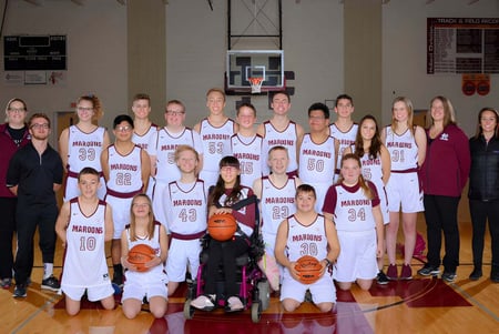 Un grupo de jóvenes jugadoras de baloncesto posan en el gimnasio de Holland Christian Schools frente a canastas de baloncesto.