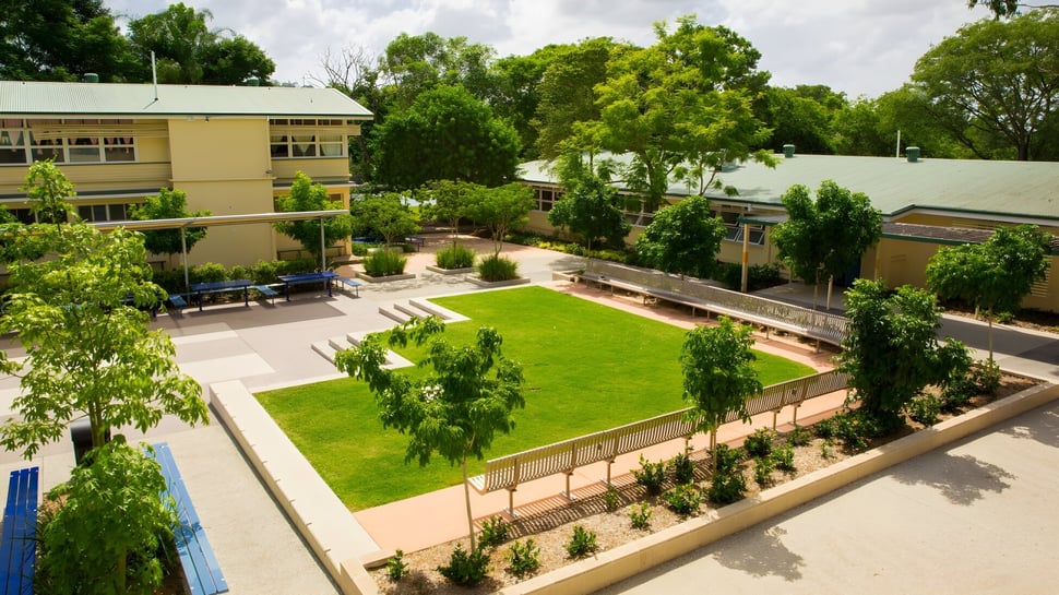 La zona verde en el campus de la Holland Park State High School muestra césped bien cuidado y vegetación circundante con un edificio al fondo.