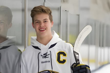 Un estudiante de la Holy Cross High School sostiene un stick de hockey y está en la pista de hielo.