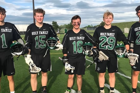 Un grupo de estudiantes de la Holy Family Catholic High School está en uniformes en un campo deportivo bajo un cielo nublado.