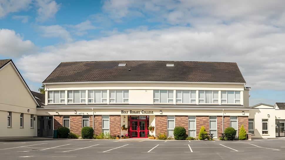 El edificio de ladrillo de dos pisos del Holy Rosary College está rodeado de un estacionamiento y paisajismo bajo un cielo nublado.