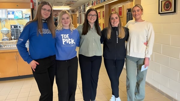 Cinco alumnas están juntas en el pasillo de la Holy Spirit High School con taquillas de fondo.