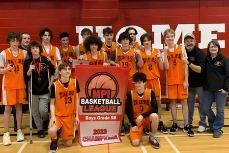 Un grupo de jóvenes jugadores de baloncesto de la Holy Trinity High School sostiene juntos un trofeo de campeonato en el gimnasio.