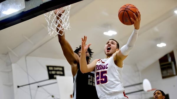 Un jugador de baloncesto con camiseta blanca salta para hacer un tiro en la cancha de baloncesto de la Hoosac School.