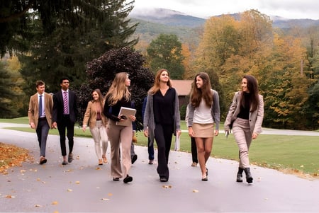 Un grupo de estudiantes de la Hoosac School da un paseo por un camino con hojas otoñales y montañas al fondo.