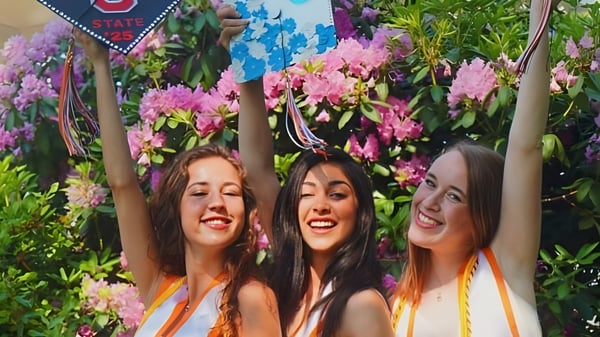 Tres alumnas de la Hopkinton High School posan frente a un colorido fondo de flores.