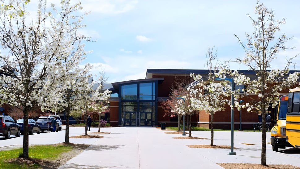 El moderno edificio de la Hopkinton High School con grandes ventanas y árboles florecientes en el exterior.