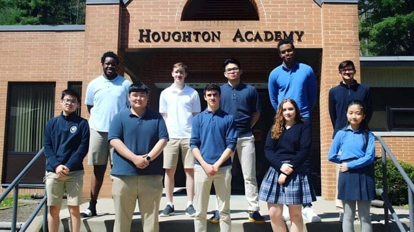 Un grupo de estudiantes está frente al edificio de Houghton Academy en uniformes escolares y posando para una foto.