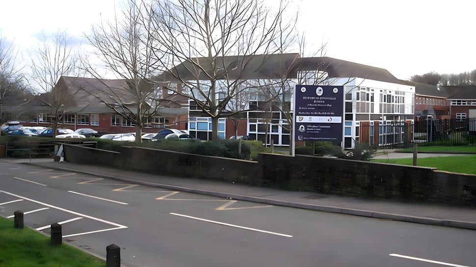 El edificio de varios pisos con entrada de vidrio de la Howard of Effingham School está rodeado de árboles desnudos y un estacionamiento.