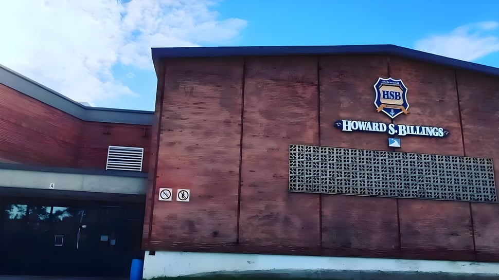 El gran edificio de ladrillo de la Howard S. Billings High School con el logo en la fachada frente a un cielo azul.