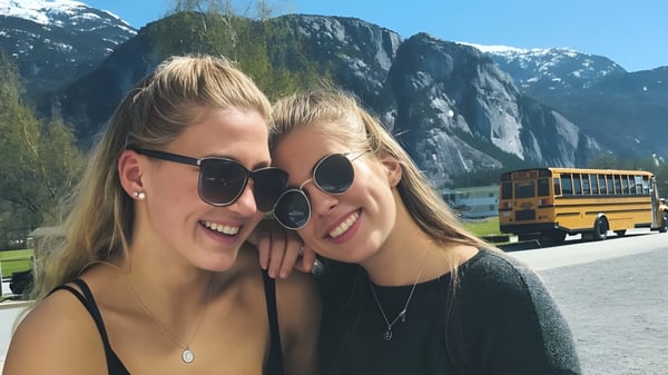 Dos alumnas con cabello rubio posan frente a un paisaje montañoso en el terreno de la Howe Sound Secondary School.