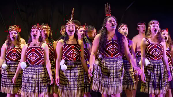 Un grupo de estudiantes de Howick College está en trajes coloridos en el escenario y canta juntos.