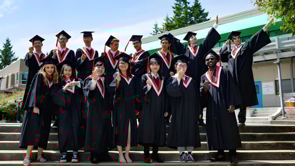 Un grupo de graduados de la Hugh Boyd Secondary School está en togas negras en las escaleras de un edificio escolar.