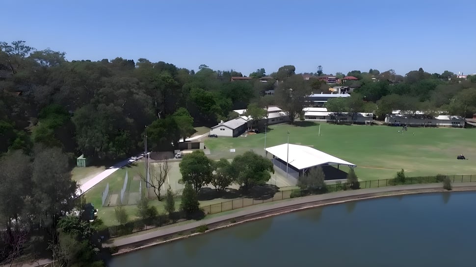 Un campo verde con un pequeño lago y edificios al fondo en el terreno de la Hunters Hill High School.