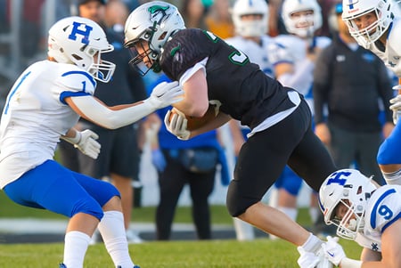 Dos jugadores en un tackle de fútbol americano en el campo de la Hunting Hills High School frente a espectadores.
