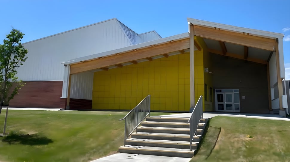 El moderno edificio de varios pisos de la Huntsville School con fachada amarilla y entrada cubierta rodeada de áreas verdes y árboles.