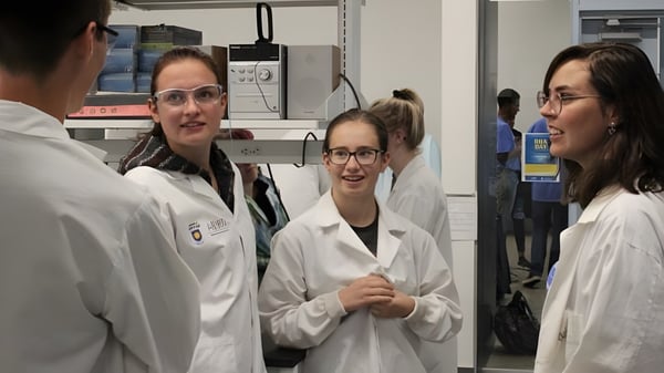 Estudiantes de la Huntsville School conversan en batas de laboratorio blancas en un laboratorio.