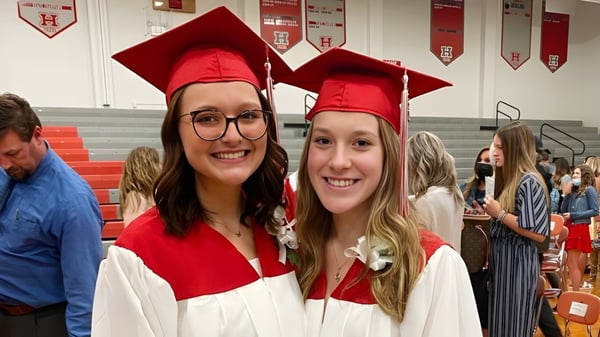 Dos estudiantes llevan birretes y togas rojas y posan en la Huron High School junto a decoraciones para la ceremonia de graduación.
