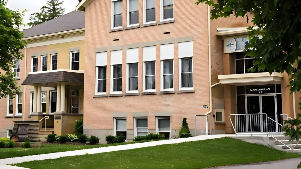 El edificio de ladrillo de varios pisos del Huron-Perth Catholic District School Board está rodeado de césped bien cuidado y árboles.