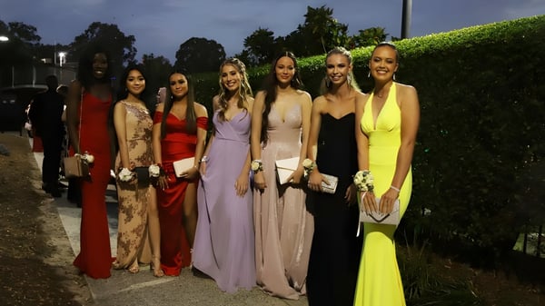 Un grupo de alumnas de Hurtwood House en elegantes vestidos de noche frente a un fondo verde por la noche.