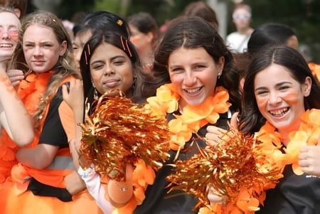 Estudiantes de Hutt Valley High School están vestidos de naranja y amarillo y muestran sus pompones durante el cheerleading en el campo.