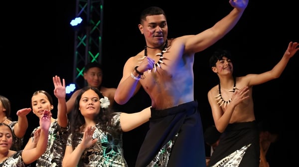 Un intérprete masculino sin camiseta está en el escenario frente a un grupo de alumnas de Hutt Valley High School con las manos levantadas.
