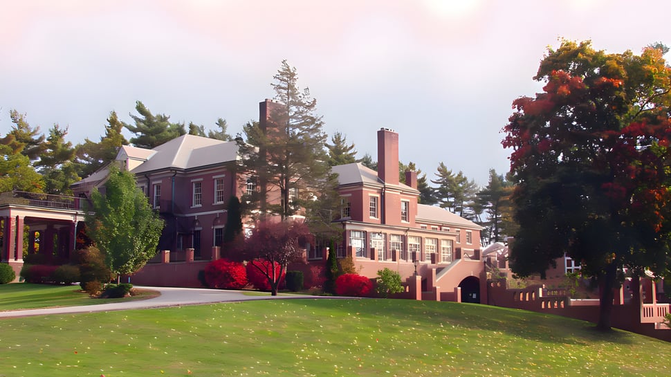 El edificio histórico de la Hyde School está rodeado de vegetación verde y coloridas hojas de otoño bajo un cielo nublado.