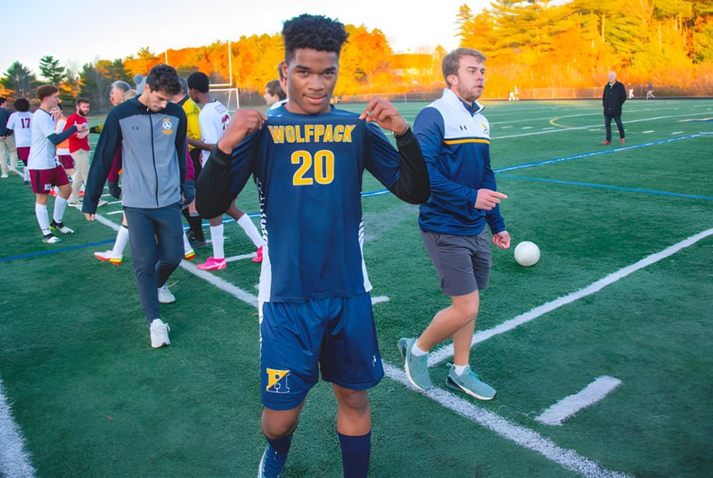 Un grupo de estudiantes de la Hyde School está vestido con ropa deportiva en el campo de fútbol con follaje otoñal de fondo.